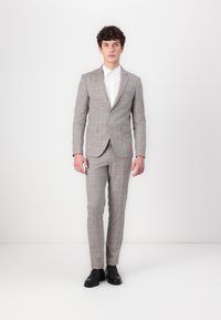 Grahamuster Anzugjacke und -hose, kombiniert mit einem weißen Hemd. Der Stoff hat eine glatte Textur. Schwarze Schuhe vervollständigen das Outfit.