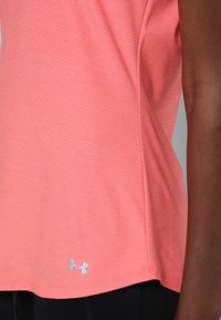 Top atlético de color rosa coral con sutiles rayas horizontales y un pequeño logotipo blanco de Under Armour cerca do do borde, combinado con leggins negros.