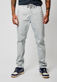 Pantalones de mezcla de lino en gris claro, con cintura ajustable, corte slim y textura sutil. Combinados con zapatillas en azul marino y crema.
