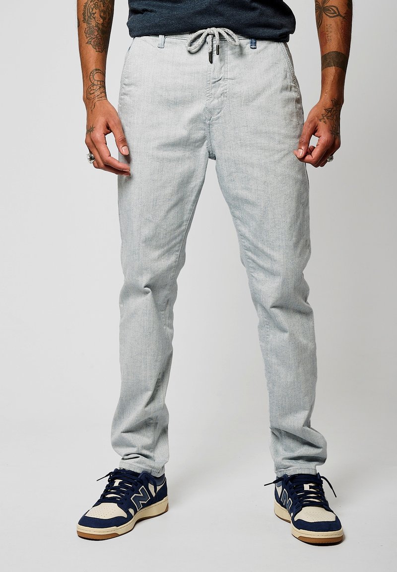Pantalones de mezcla de lino en gris claro, con cintura ajustable, corte slim y textura sutil. Combinados con zapatillas en azul marino y crema.
