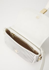 Borsa a tracolla bianca in pelle con design perforato, hardware dorato e tasca interna con zip. L'interno è foderato con un tessuto beige a contrasto.