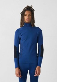 Maglia sportiva a maniche lunghe di un blu intenso con colletto alto, pannelli laterali neri a contrasto e dettagli testurizzati. Design liscio e aderente.