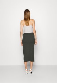 Ribbed, dark green midi skirt with a fitted waistband, paired with a light gray tank top and white heeled sandals. View from the back.