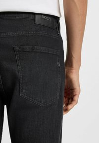 Jeans in denim nero con una tasca posteriore e un'etichetta in pelle impressa con "BOSS". Il tessuto è liscio con una leggera lucentezza.