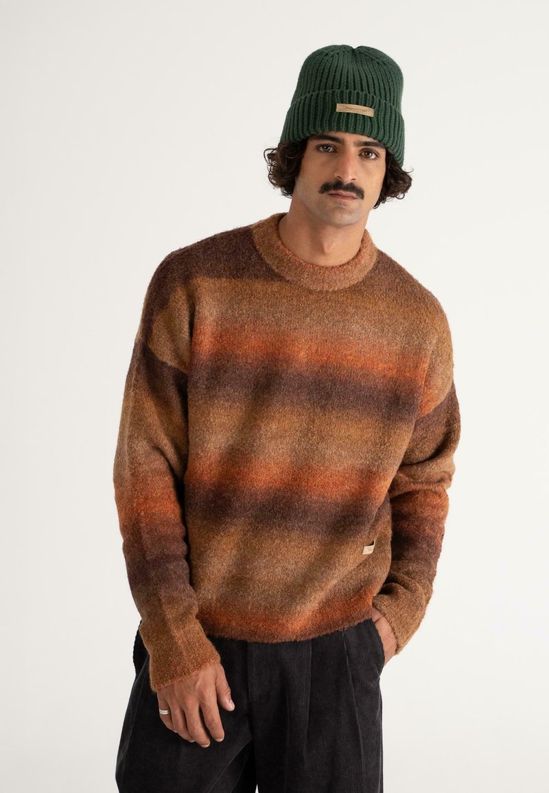 Strickpullover in braun, orange und lila Streifen; runder Halsausschnitt; weiche Textur; kombiniert mit einer grünen Rippmütze; dezentes Logo-Detail.