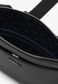 Borsa nera in tessuto con chiusura a zip; l'interno presenta una fodera scura a motivo e una tasca con zip aggiuntiva per l'organizzazione.