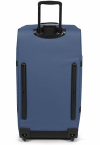 Maleta rígida azul con mango retráctil, acentos de goma negra, ruedas dobles y asas laterales discretas para un fácil levantamiento.