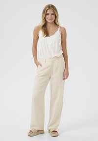 Débardeur blanc léger avec bordure en dentelle, associé à un pantalon large en lin beige et des sandales à plateforme tissées. Design simple et élégant.