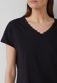 Chemise noire à manches courtes avec un décolleté en V orné de dentelle noire en forme de vagues. Tissu doux, coupe décontractée et détails minimalistes.