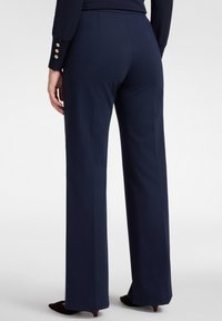 Marineblauwe broek met een getailleerde pasvorm, voorzien van een recht ontwerp en zijzakken. Heeft een zachte textuur en subtiele plooien.