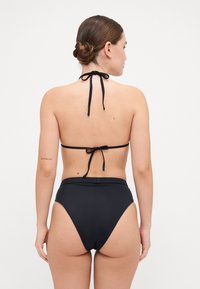 Svart bikinitopp med halterneck-bånd og høyhånds nederdel, glatt tekstur, minimalistisk design og subtile detaljer.