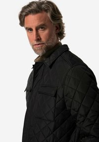 Černá prošívaná bunda s límečkem, dvěma hrudními kapsami a texturovaným povrchem. Design zahrnuje šití ve tvaru diamantů.