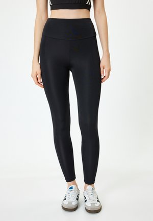 Leggings noirs en tissu extensible, avec une taille haute et une coupe ajustée. Portés avec des baskets décontractées. Apparence simple et épurée.
