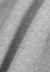 Lichtgrijze stof met een zachte textuur, voorzien van een glad, licht glanzend oppervlak en een subtiel, uniform weefpatroon.