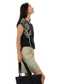 Zwart T-shirt met korte mouwen met een bloemenborduurontwerp, gecombineerd met beige shorts. Het model houdt een zwarte tote bag vast. Effen witte achtergrond.