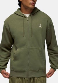 Felpa con cappuccio color oliva con zip frontale, tasca anteriore, cappuccio con coulisse e logo Jumpman bianco sul petto. Realizzata in tessuto morbido con una trama semplice.