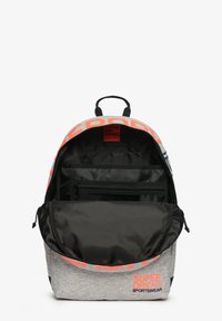 Mochila gris con detalles en naranja, con apertura en la parte superior y un interior negro. Cuenta con un compartimento con cremallera y detalles del logo en el exterior.