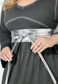 Vestito grigio con scollatura a V e maniche lunghe, stretto in vita da una cintura argentata lucida annodata a fiocco. Tessuto liscio e morbido.