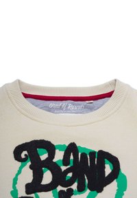 Beige collegepaita, jossa on ribattu kaula-aukko; sisältää mustaa pörröistä kirjainpainatusta, jossa lukee "BAND" vihreän pyöreän kuvion päällä; punainen sisäkaulus.