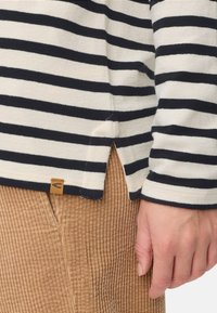 Langsleeve gestreepte shirt in marineblauw en crèmekleur, met een zijsplit en een tan kleurig label, gecombineerd met gestructureerde corduroy broek.