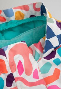 Kolorowa podszewka kurtki z turkusowym polarem, z zewnętrznym wzorem abstrakcyjnych kształtów w różowym, niebieskim i pomarańczowym.