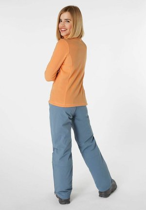 Oranges Fleece Langarmshirt mit strukturiertem Stoff und blauen wasserdichten Hosen. Die Hose hat einen Reißverschluss am unteren Bein und robuste schwarze Stiefel.