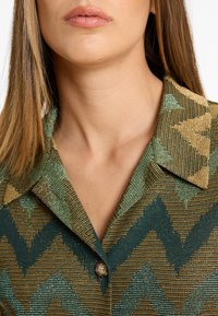 Hemd mit Kragen, das ein strukturiertes, mehrfarbiges Zickzackmuster in Grün, Gold und Bronze aufweist, mit einem einzelnen Knopfdetail.