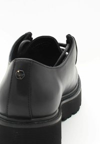 Chaussure en cuir noir avec un talon bas, un bout rond et une semelle en caoutchouc texturé. Présente un accent métallique à l'arrière et des détails de coutures.