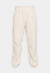 Cream-colored sweatpants with an elastic waistband, tapered cuffs, and a small white logo on the left thigh. Made from soft fabric.