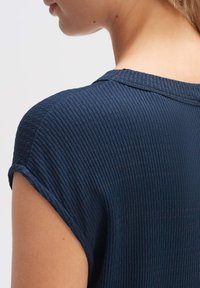 Top a coste blu navy con scollatura rotonda e maniche corte arrotolate. Il tessuto presenta una texture sottile con righe orizzontali.