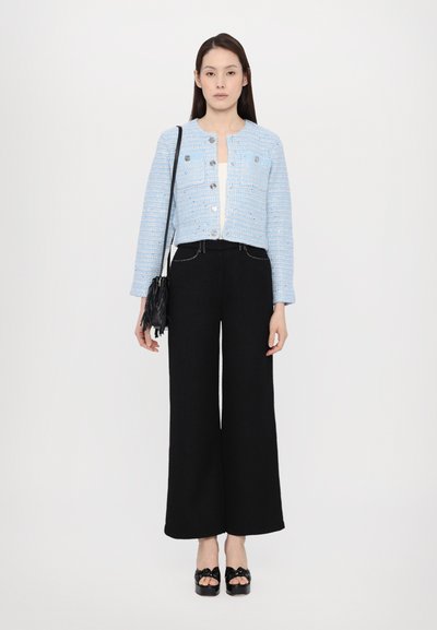 Light blue cropped tweed jacket with silver buttons, paired with high-waisted black wide-leg trousers. Model carries a black fringe handbag.