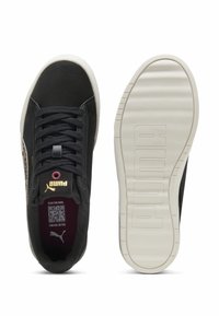 Zapatillas negras con un diseño texturizado, que cuentan con un logo dorado, cordones y una suela de goma blanca en contraste con la marca embossada.