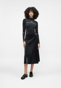 Top preto de mangas longas com detalhes em cinza, combinado com uma saia de couro preta de comprimento médio com uma superfície texturizada e detalhe com fivela lateral. Sapatos pretos.