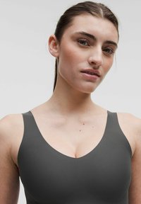 Pelēks sporta krūšturis ar platām siksnām, gludu tekstūru un noapaļotu dekoltē. Minimalistisks dizains bez redzamām detaļām vai rakstiem.