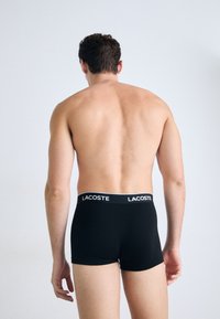 Zwarte korte boxershorts met een wit Lacoste-logo op de tailleband, gemaakt van een gladde, elastische stof en een aansluitende pasvorm.