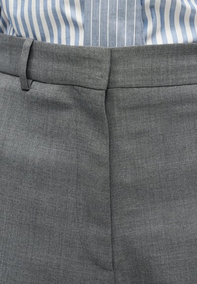 Gros plan sur la taille d'un pantalon gris sur mesure avec passants de ceinture, porté avec une chemise rayée bleue et blanche rentrée.