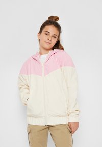 Hooded vindjacka i krämfärgad och rosa med blixtlås framtill, elastiska ärmslut och en färgblockdesign. Slät tygtextur.