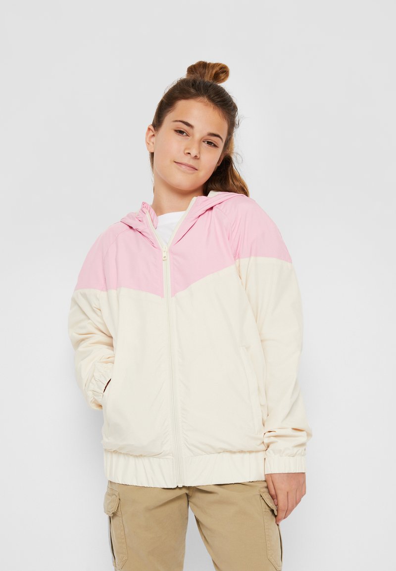 Hooded vindjacka i krämfärgad och rosa med blixtlås framtill, elastiska ärmslut och en färgblockdesign. Slät tygtextur.