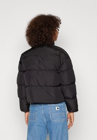 Svart puffjakke med en kort design, med kvilte seksjoner og en glatt tekstur. Brukt over lyseblå jeans med et logo-merke.
