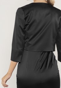 Svart satin cropped jacka med trekvartsärmar, med en slät yta och ett enkelt mönster, kombinerad med en svart klänning.
