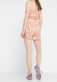 Kevyt, vaaleanpunainen urheil bra, jossa on leikkaussuunnittelu ja samansuuntaiset satiinishortsit. Varustettu joustavalla vyötäröllä ja heijastavalla yksityiskohdalla. Kirkkaat kengät.