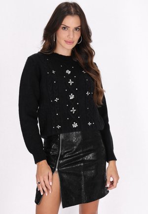 Maglione corto nero con motivo a treccia e decorazioni floreali argentate. Abbinato a una gonna in pelle nera lucida con zip laterale.