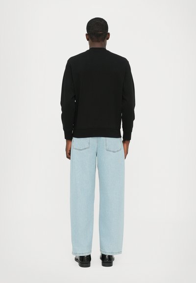 Sweatshirt noir à col rond et poignets côtelés, associé à un jean taille haute en denim clair. Design simple sans logos visibles.