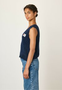 Marineblauw, mouwloos gebreid vest in zachte textuur met een licht cropped ontwerp. Voorzien van een klein, kleurrijk logo op de voorkant.