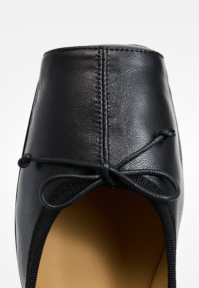 Ballerina nera in pelle liscia. Presenta una punta arrotondata, un bordo elasticizzato e un fiocco decorativo con dettagli cuciti.