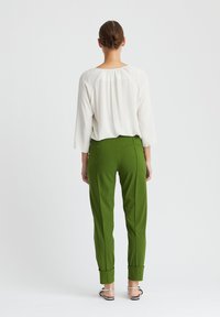 Weiße Bluse mit gefaltetem Rücken und dreiviertel Ärmeln, kombiniert mit grünen maßgeschneiderten Hosen mit umgeschlagenen Säumen und Gesäßtaschen.