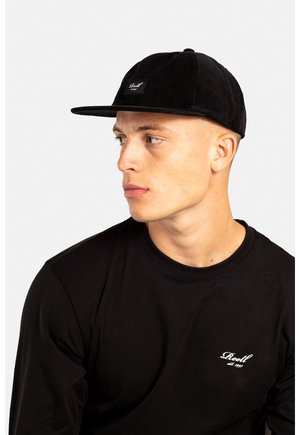 Schwarze Cord-Hut mit flachem Schirm und kleinem Logo-Patch. Getragen mit einem enganliegenden schwarzen Langarmshirt. Sauberes Design, strukturiertes Material.