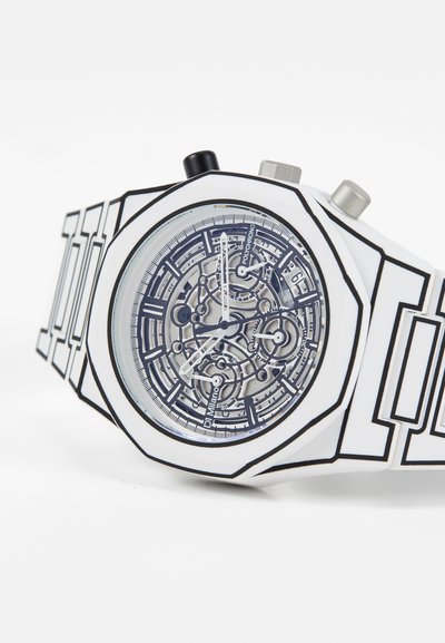 Hvidt ur med geometrisk design, gennemsigtig skive der afslører indviklede mekanismer, sorte accenter og sølvfarvede knapper på siden.