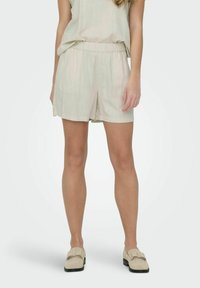Lichtbeige shorts met een elastische tailleband, gemaakt van een gestructureerde, geweven stof. Gecombineerd met een bijpassende losse top en lichte schoenen.