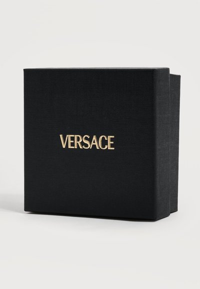 Boîte de luxe noire texturée avec logo doré "VERSACE" centré à l'avant, légèrement ouverte sur le côté droit sur fond blanc.